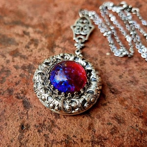 May include: A silver locket necklace featuring a red and blue iridescent opal stone set in a filigree design.