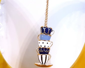 May include: A gold chain necklace with a charm of four stacked teacups. The teacups are decorated with blue and white patterns.