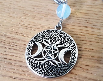 May include: Silver necklace with a circular pendant featuring a triple moon and pentacle design. The pendant is surrounded by a Celtic knot pattern. The necklace also includes a light blue bead.