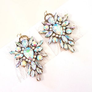 Peut inclure: Une paire de boucles d'oreilles en cristal iridescent avec une finition dorée. Les boucles d'oreilles ont la forme d'une fleur avec un cristal en forme de larme au centre.