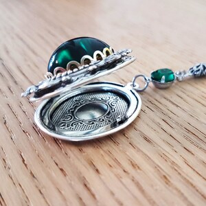May include: A silver locket necklace with a green gemstone and ornate detailing. The locket is open, revealing a blank interior.