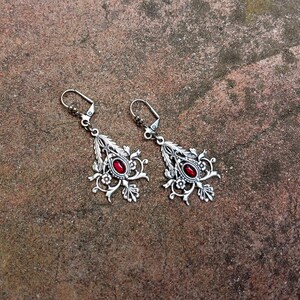 May include: A pair of silver earrings with intricate floral designs and red gemstone accents.