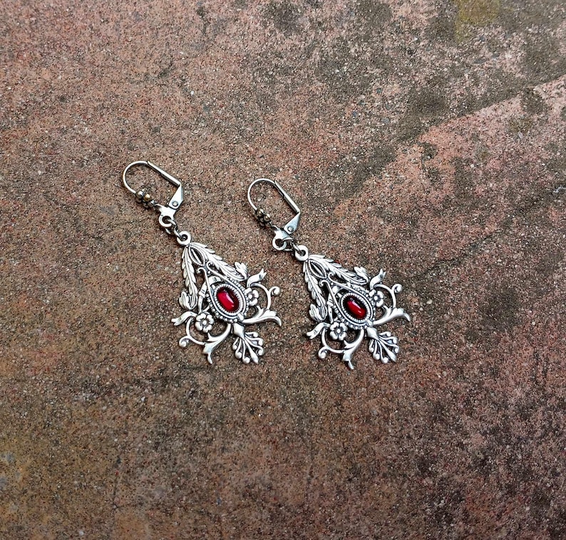 May include: A pair of silver earrings with intricate floral designs and red gemstone accents.