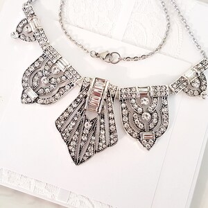 Puede incluir: Un collar de plata con un dise&ntilde;o geom&eacute;trico que presenta m&uacute;ltiples colgantes incrustados con cristales.