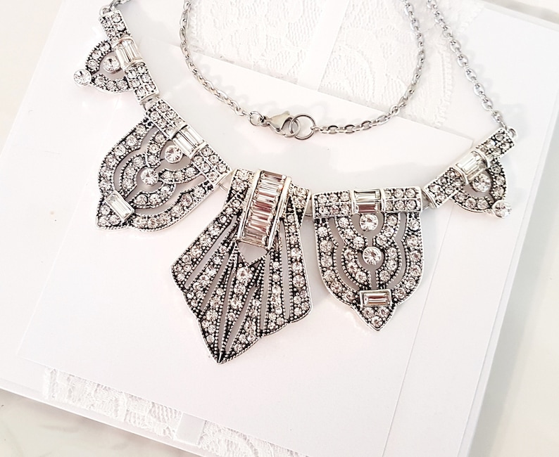 Puede incluir: Un collar de plata con un dise&ntilde;o geom&eacute;trico que presenta m&uacute;ltiples colgantes incrustados con cristales.