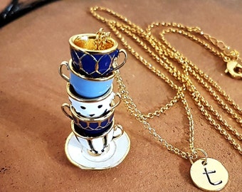 May include: A gold chain necklace with a charm of a stack of four miniature teacups with blue and white patterns. The charm is on a white saucer. The necklace also has a small gold charm with the letter 't' on it.