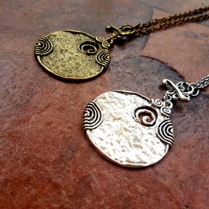 May include: Two silver and bronze necklaces with round pendants featuring a textured surface and a swirling design.