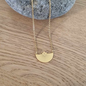 May include: A gold necklace with a geometric sunburst pendant. The pendant is a half-circle with a diamond shape in the center.