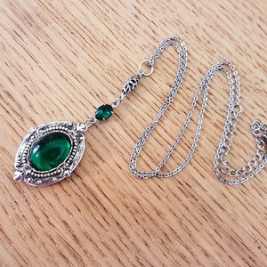 May include: A silver necklace with a green gemstone pendant. The pendant is oval shaped and has a detailed filigree design. The chain is a delicate silver chain.