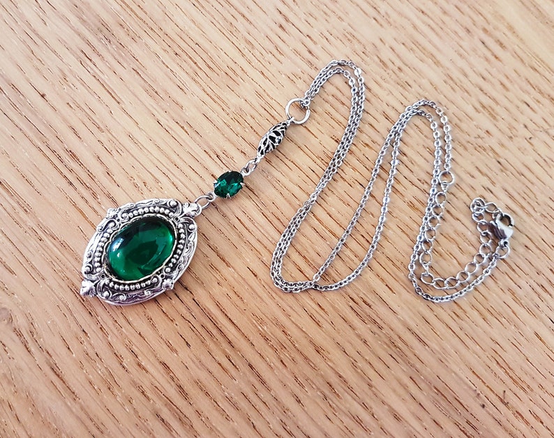 May include: A silver necklace with a green gemstone pendant. The pendant is oval shaped and has a detailed filigree design. The chain is a delicate silver chain.