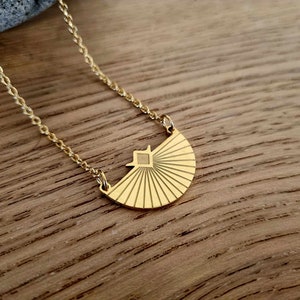 May include: A gold necklace with a geometric sunburst pendant. The pendant is made of metal and has a textured surface.