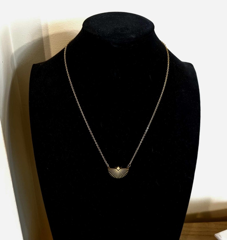 May include: A gold chain necklace with a geometric sunburst pendant.