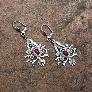 May include: A pair of silver earrings with red gemstone accents. The earrings feature a delicate floral design.