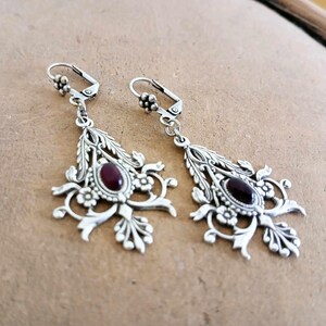 May include: A pair of silver dangle earrings with intricate floral designs and a dark red gemstone in the center of each earring.