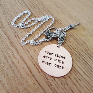 Pode incluir: Colar de prata com um pingente redondo de cobre gravado com as palavras "ever thine ever mine ever ours". O colar tem uma corrente delicada e detalhes florais.