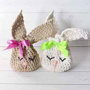 May include: Two crocheted bunny-shaped gift bags. One is beige with a pink bow and the other is white with a green bow. Both have embroidered eyes and a pink nose.