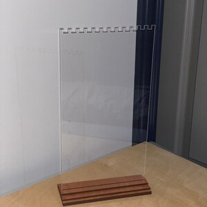May include: A clear acrylic earring display stand with a wooden base. The stand has multiple rows of holes for holding earrings.