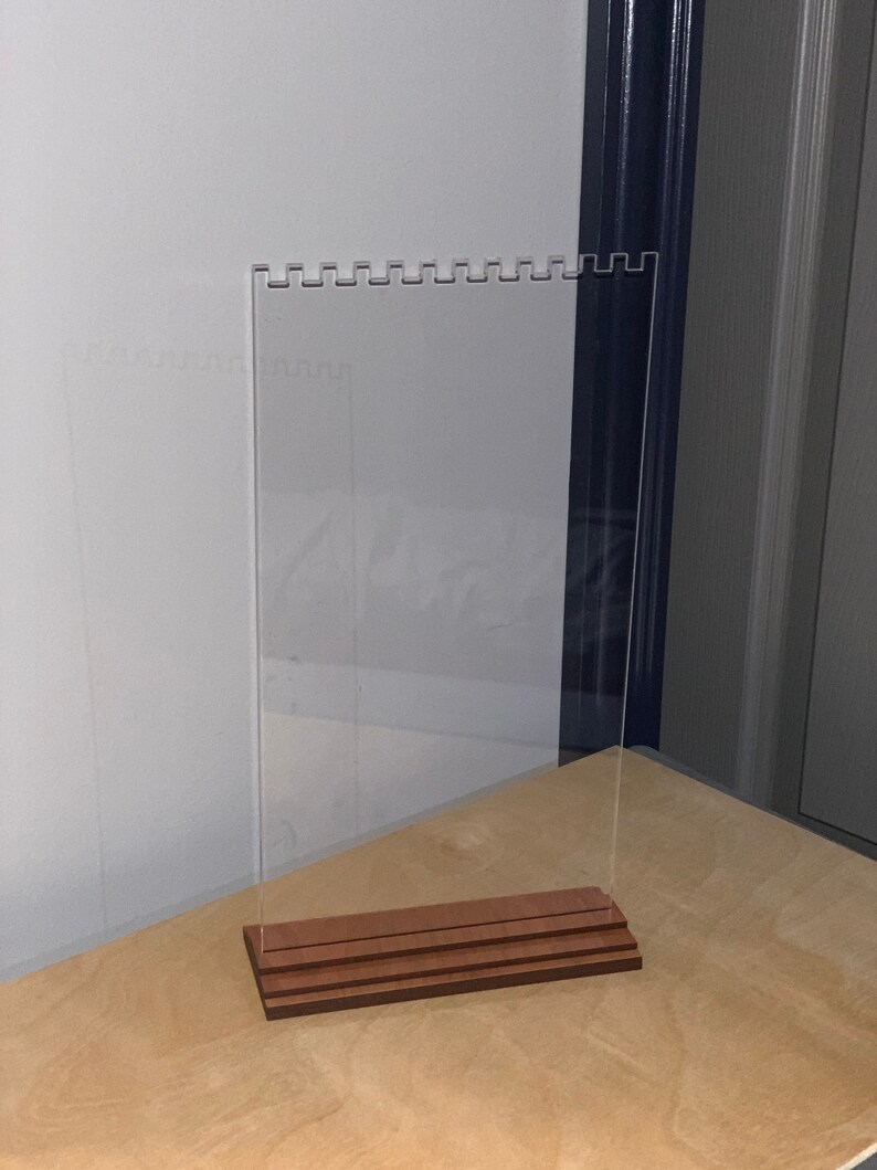 May include: A clear acrylic earring display stand with a wooden base. The stand has multiple rows of holes for holding earrings.