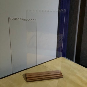 May include: A clear acrylic display stand with a wooden base. The stand has a scalloped edge and is designed to hold jewelry or other small items.