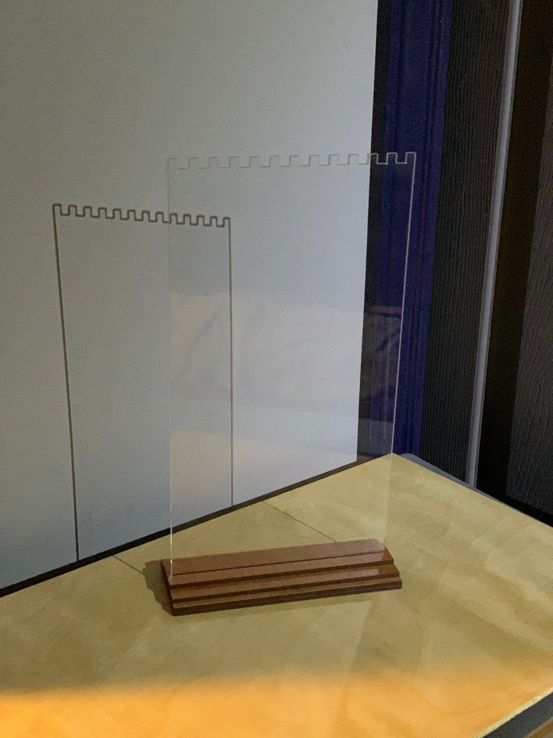 May include: A clear acrylic display stand with a wooden base. The stand has a scalloped edge and is designed to hold jewelry or other small items.