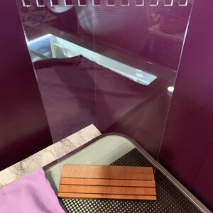 May include: A clear acrylic sign holder with a wood base. The base has three horizontal grooves. The sign holder has a scalloped top edge.
