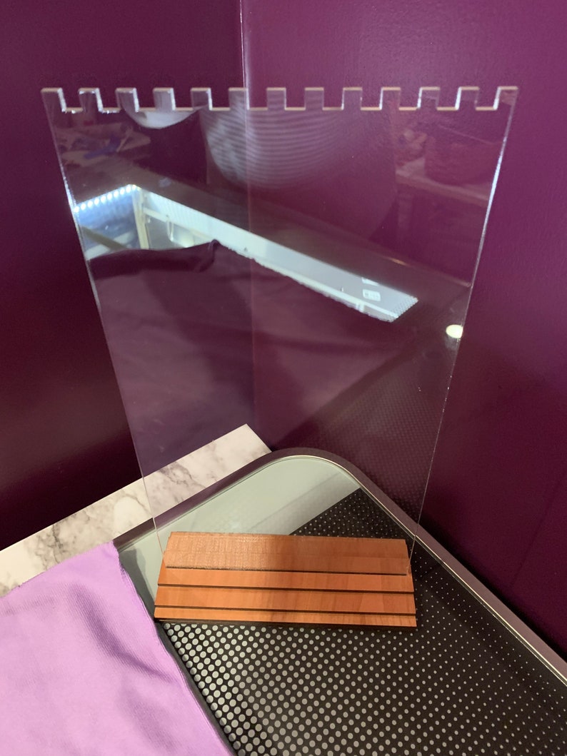 May include: A clear acrylic sign holder with a wood base. The base has three horizontal grooves. The sign holder has a scalloped top edge.