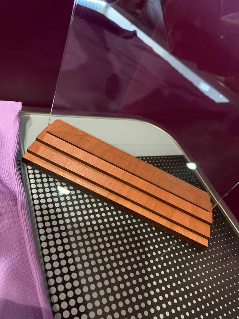 May include: A clear acrylic display stand with a wooden base. The base is made of three layers of wood, each with a different grain pattern. The stand is sitting on a black surface with white polka dots.