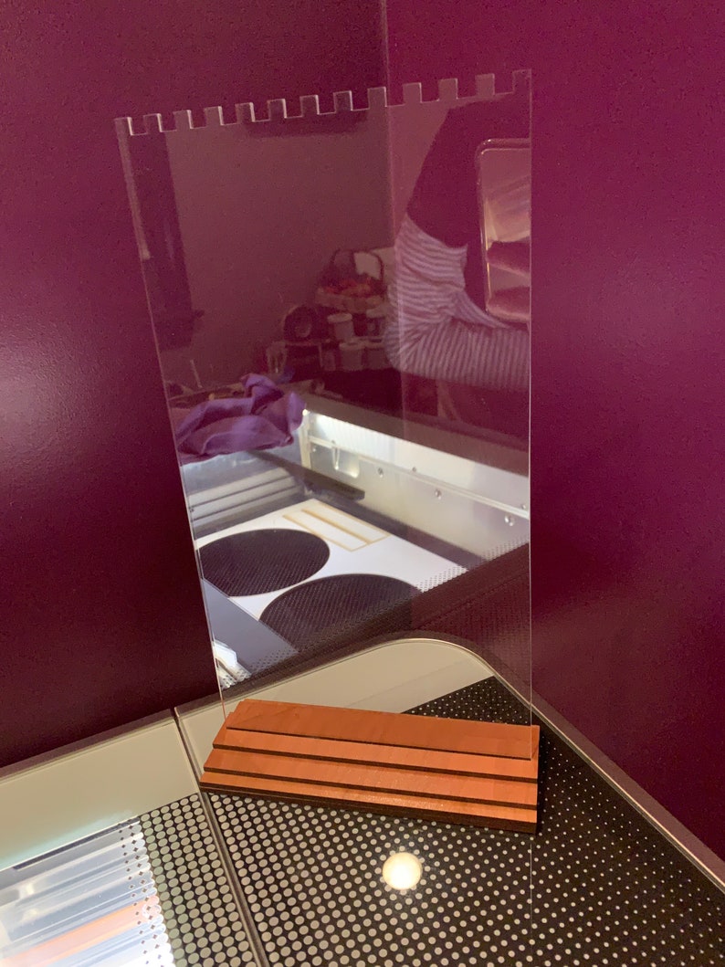 May include: A clear acrylic sign holder with a wood base. The sign holder has a scalloped top edge and is standing on a table with a black and white patterned surface.