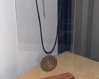 May include: A wooden pendant necklace with a detailed mandala design hangs on a clear acrylic display stand with a wooden base.