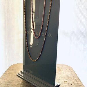 May include: A gray display stand with two gold chains hanging from it. The stand has a logo that reads "OCEDA & CO."