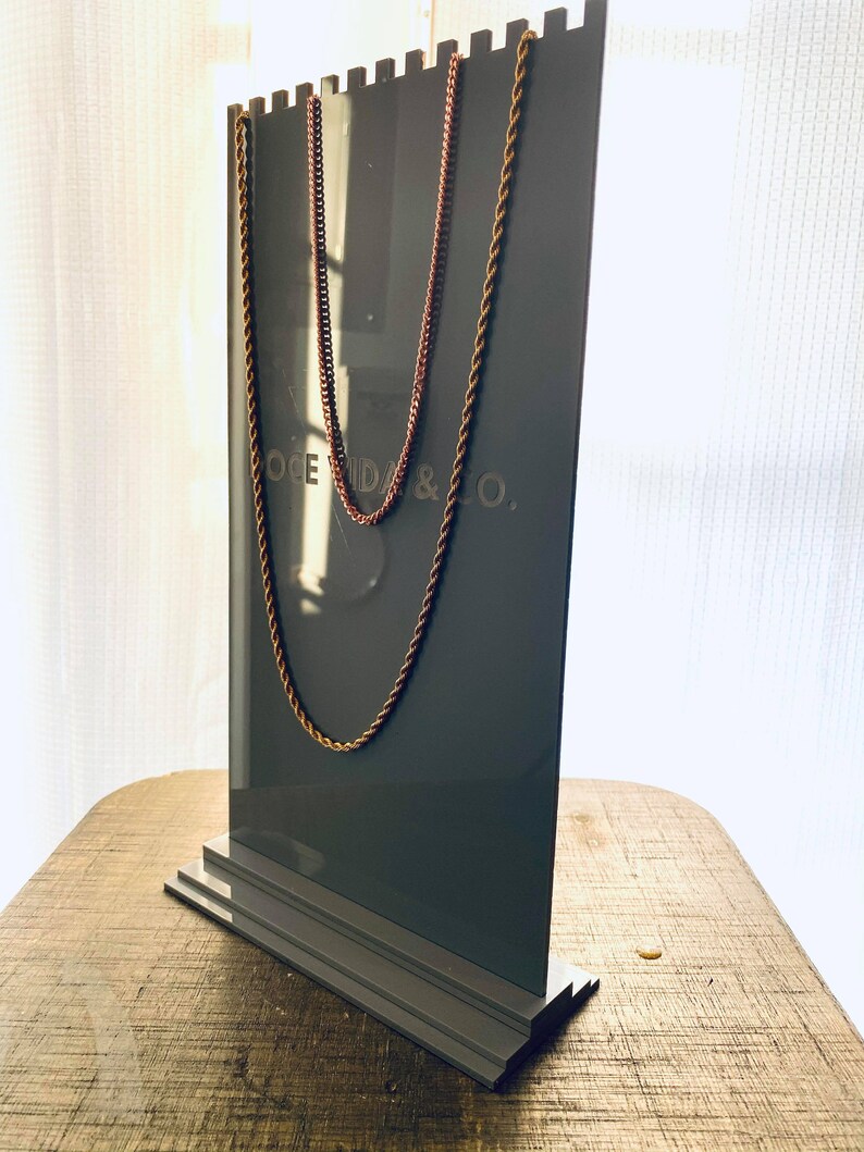 May include: A gray display stand with two gold chains hanging from it. The stand has a logo that reads "OCEDA & CO."