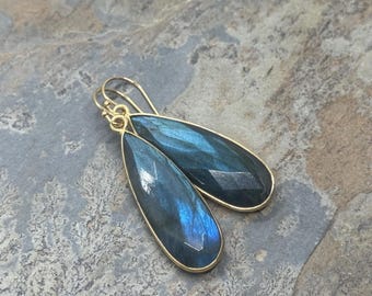 Op de afbeelding: Een paar gouden oorhangers met traanvormige labradoritsteen. De stenen zijn diepblauw met iriserende kleurvlekken.
