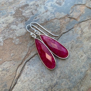 May include: A pair of silver dangle earrings with teardrop-shaped red gemstone stones.