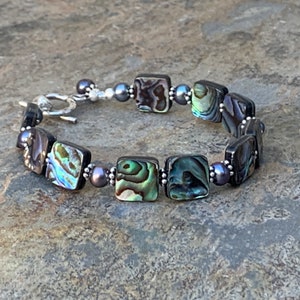 May include: A bracelet made with square abalone shell beads and silver beads. The bracelet has a silver clasp.