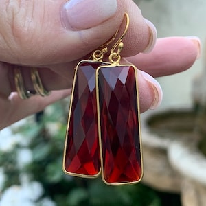 Puede incluir: Un par de pendientes de aro de oro con piedras preciosas rectangulares facetadas de color rojo oscuro.
