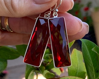 Op de afbeelding: Een paar zilveren oorhangers met rechthoekige rode edelsteen druppels. De oorbellen hebben een facetgeslepen ontwerp en zijn diep rood van kleur.