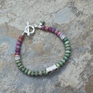 Op de afbeelding: Een veelkleurige edelsteen armband met een zilveren toggle sluiting en een zilveren tonvormige kraal. De armband heeft roze, groene en witte edelstenen.