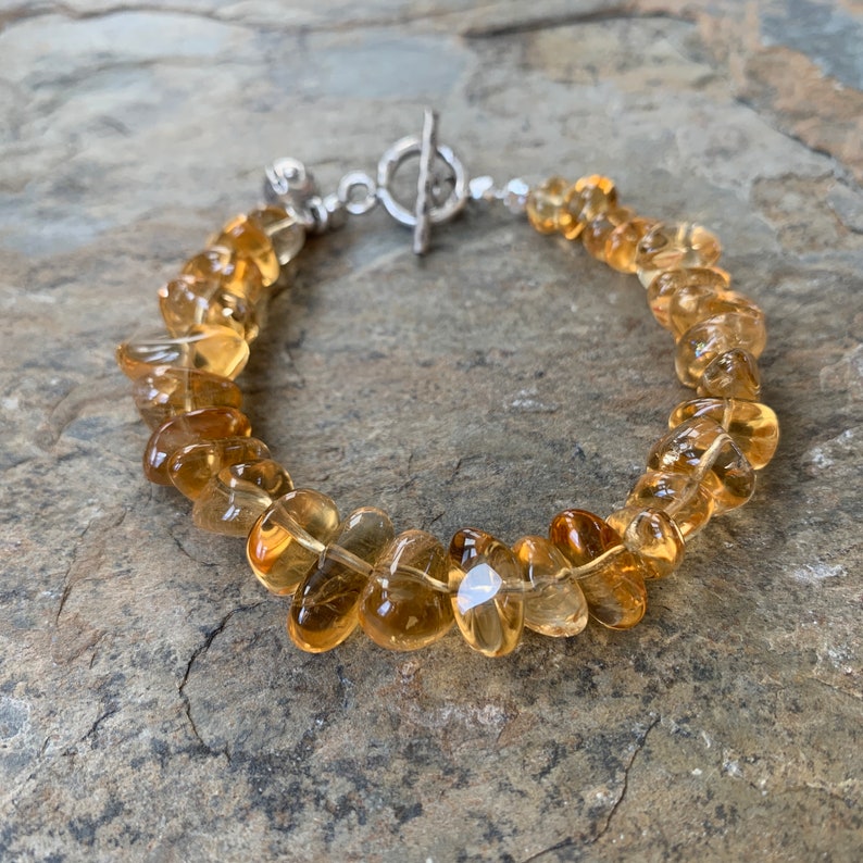 May include: A gold and brown gemstone bracelet with a silver toggle clasp. The bracelet is made of smooth, rounded stones.