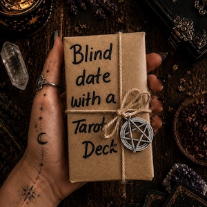 Puede incluir: Una baraja de tarot rectangular envuelta en papel kraft marr&oacute;n, atada con cuerda natural y con un dije de pent&aacute;culo plateado. El texto 'Blind date with a Tarot Deck' est&aacute; escrito con tinta negra en el frente del envoltorio de papel.