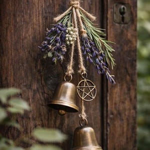 May include: A rustic door decoration featuring two bronze bells, a pentagram charm, and sprigs of lavender and greenery, all suspended by twine. The wooden door has a dark, aged appearance.