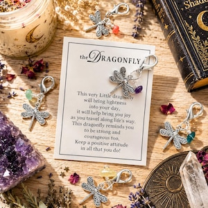 May include: Five silver-toned dragonfly charms with lobster clasps, each accented with a small colorful gemstone bead. The charms are displayed on a white card featuring the text: the Dragonfly, This very Little dragonfly will bring lightness into your day.