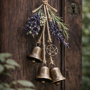May include: A rustic hanging decoration featuring three bronze bells suspended from twine, adorned with lavender, greenery, and a pentagram charm. The arrangement is set against a weathered wooden door, creating a natural, earthy aesthetic.