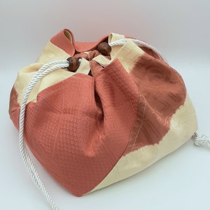 May include: A red and cream fabric drawstring bag with wooden toggles. The bag is made of a patterned fabric and has a gathered top.