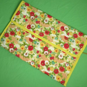 May include: A yellow fabric pouch with a floral pattern featuring red, yellow, and white flowers. The pouch has a yellow zipper and a quilted design.