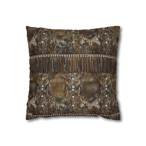 May include: Square decorative pillow with a brown and gold embossed pattern. The pillow features a fringe detail and is embellished with small, sparkling rhinestones. The design has a vintage, ornate aesthetic.