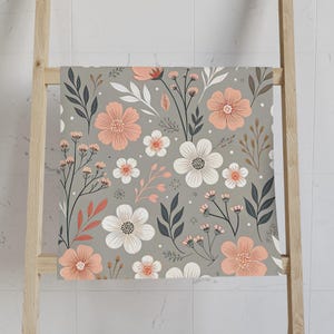 May include: A gray floral patterned towel with a wooden ladder. The towel features a repeating pattern of peach and white flowers, dark gray leaves, and small pink accents. The towel is displayed on a light brown wooden ladder.