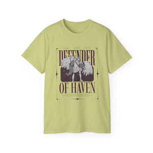 May include: A light green t-shirt featuring a graphic of an angel with wings, holding a sword. The text "DEFENDER OF HAVEN" is displayed in a rectangular frame. The shirt is made of a soft material.