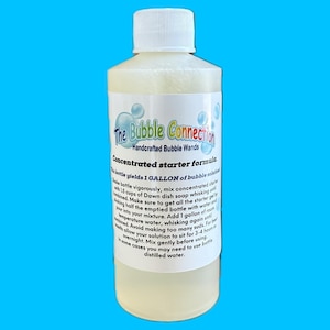 May include: A clear plastic bottle filled with a pale yellow concentrated bubble solution. The white label features the text The Bubble Connection Handcrafted Bubble Wands and instructions for mixing the formula to yield 1 gallon of solution.