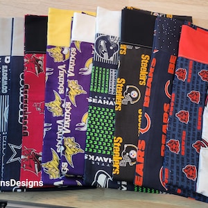 May include: A collection of fabric strips featuring various NFL team logos, including the Lions, Cowboys, Vikings, Seahawks, Steelers, Falcons, and Packers. The fabric is a mix of blue, red, green, white, and black.