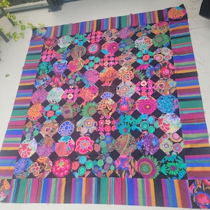 May include: A large rectangular quilt featuring a central grid of multicoloured floral and geometric patterned octagons set against a black background, framed by a wide border of vibrant, multi-coloured horizontal stripes in various widths.